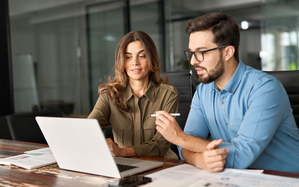 Two busy colleagues working together talking using laptop in office